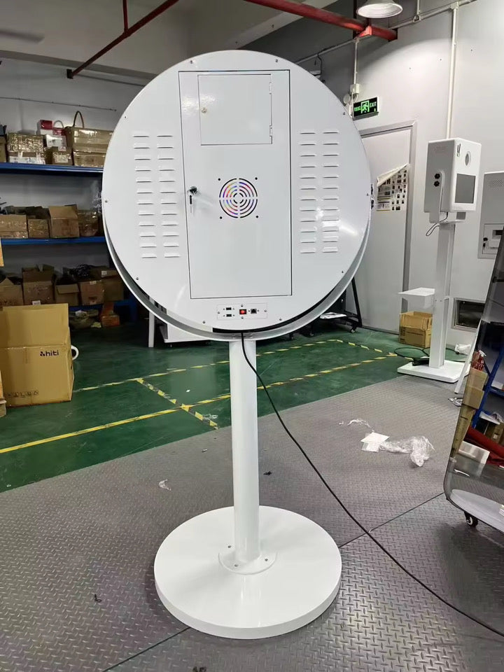 A round magic mirror photobooth with a colorful LED light ring around the mirror, mounted on a stand, with a mini PC and camera attached.