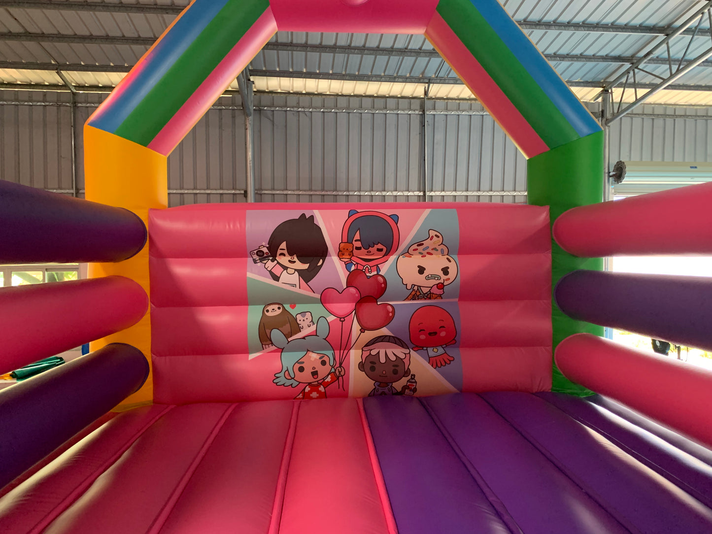 Colorful inflatable bounce house with cartoon character graphics on a metal roofed area.