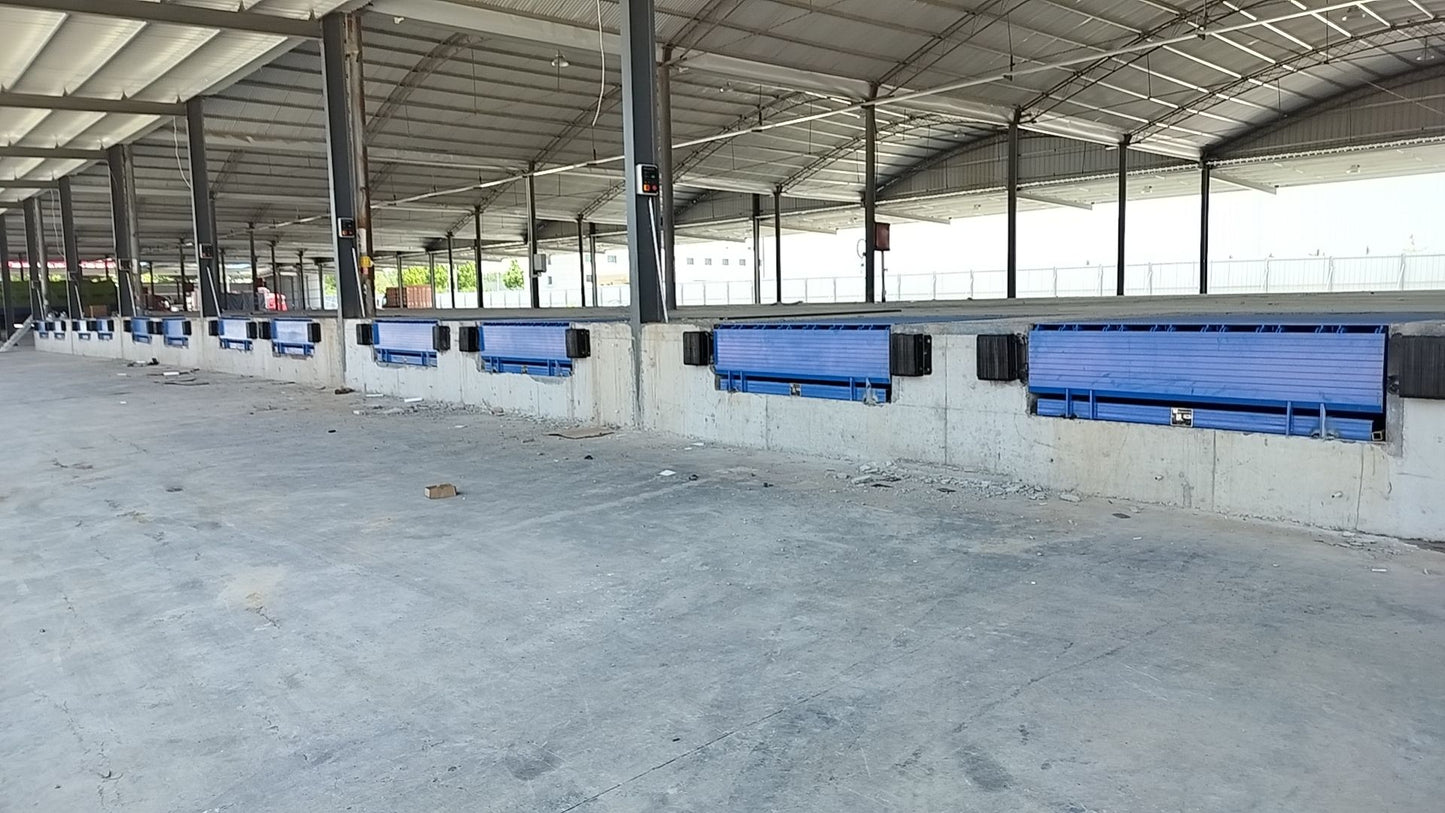 Large outdoor area with rows of blue Hydraulic telescopic dock leveler under a metal roof.