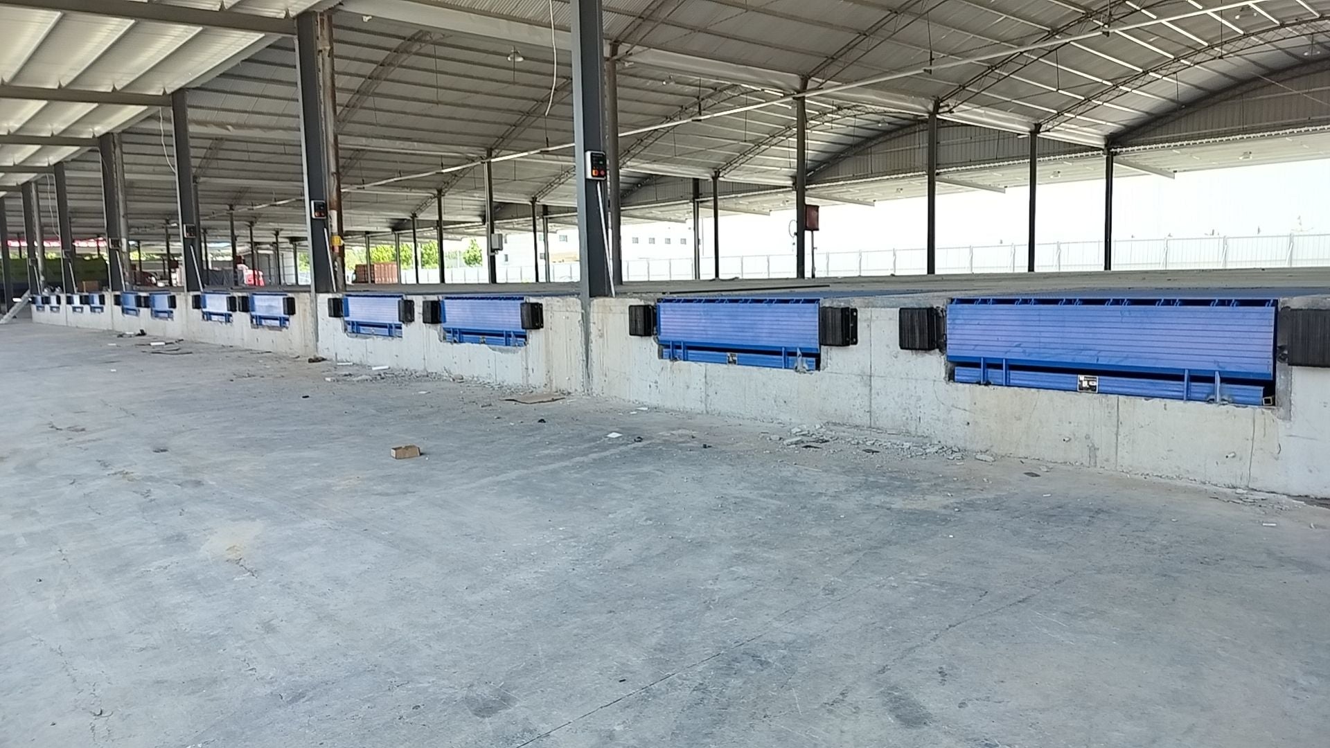 Large outdoor area with rows of blue Hydraulic telescopic dock leveler under a metal roof.
