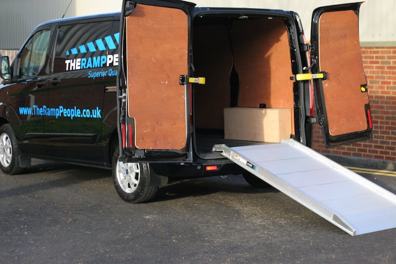 Van with open doors and a ramp, loaded with boxes, in front of a building.