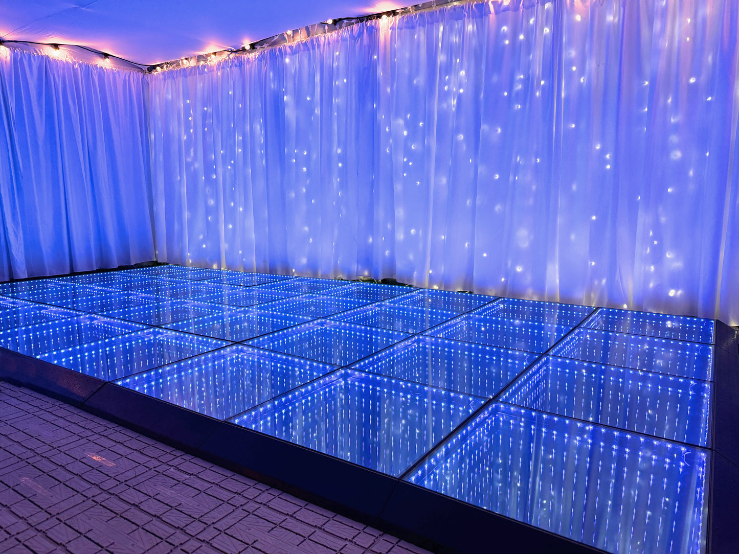LED dance floor with blue lighting in a room with white curtains and string lights.