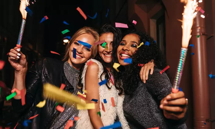 Three women celebrating with confetti and sparklers at a party in a picture taken. by a photobooth