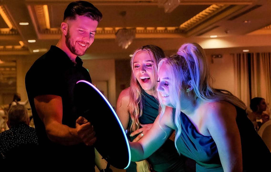 Three people interacting with a Roamer IPad Photobooth LED Ring Lighting in an indoor setting