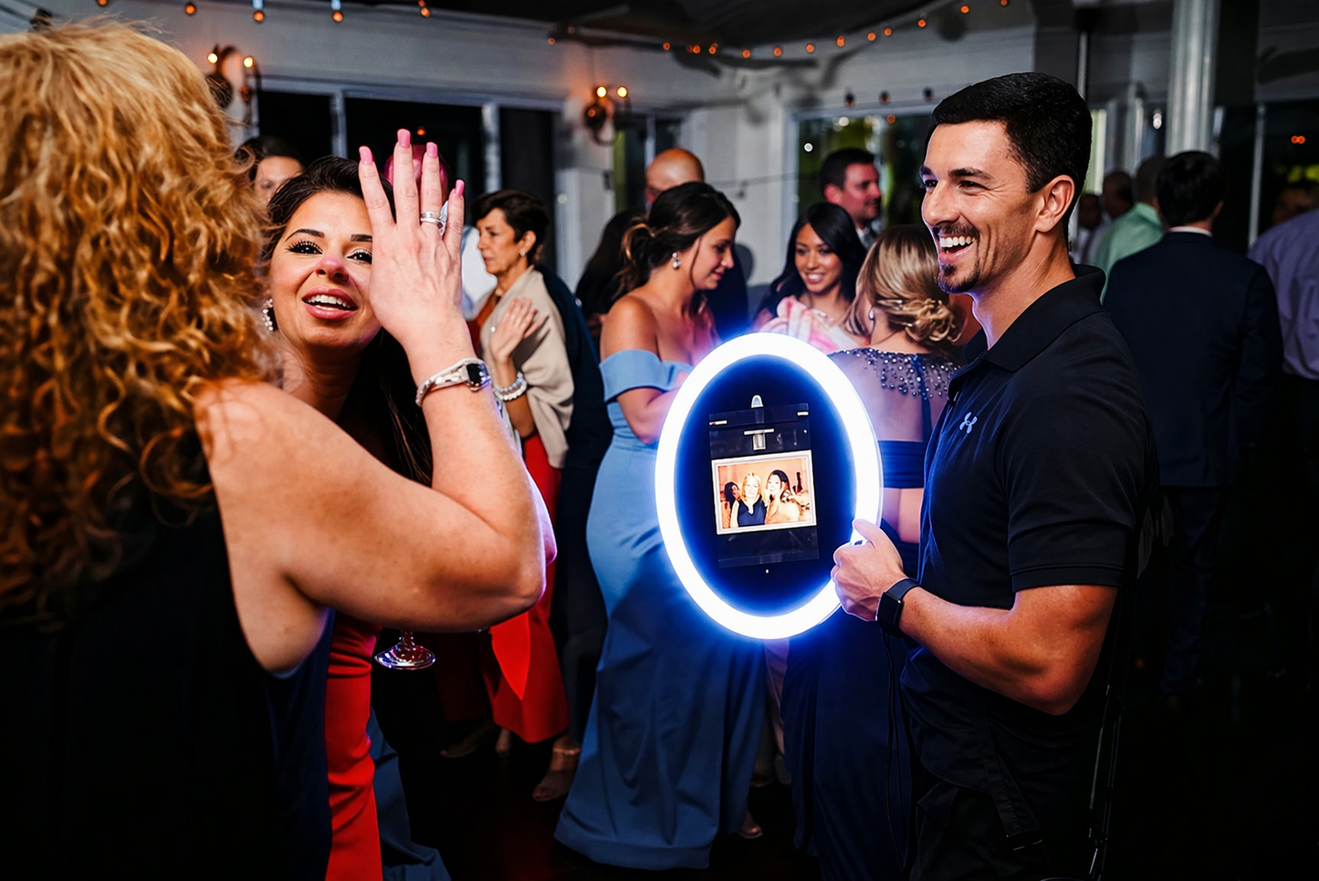 Man holding a Roamer IPad Photobooth LED Ring Light with a photo of a couple, with people in the background at a party.
