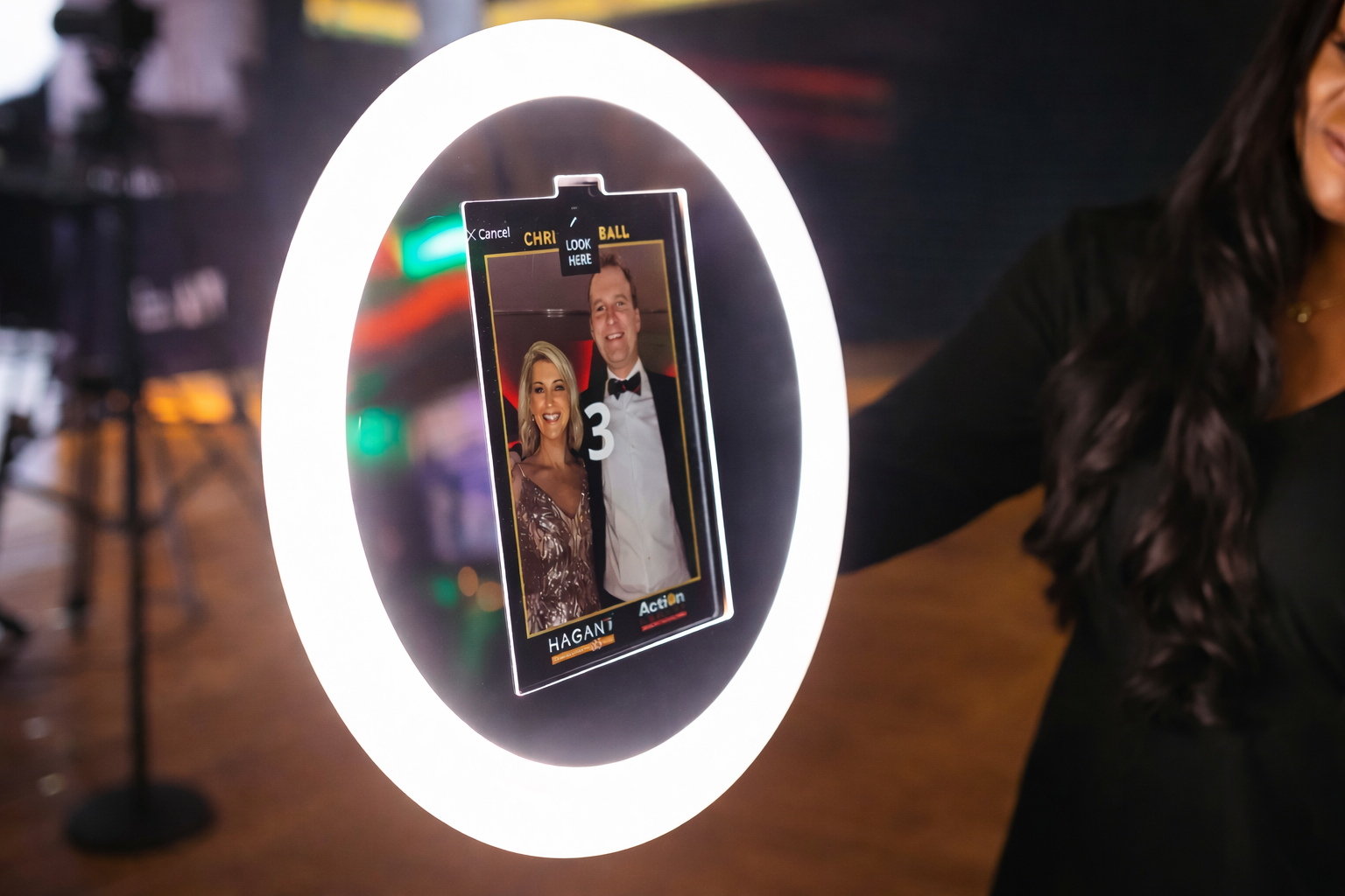 Person holding a Roamer IPad Photobooth LED Ring Light with a photo of a couple and text, illuminated by a ring light.