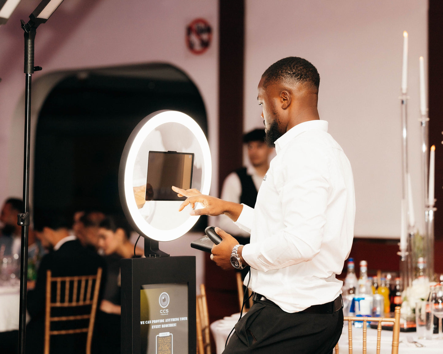 Man adjusting a ring light at an event with blurred attendees in the background