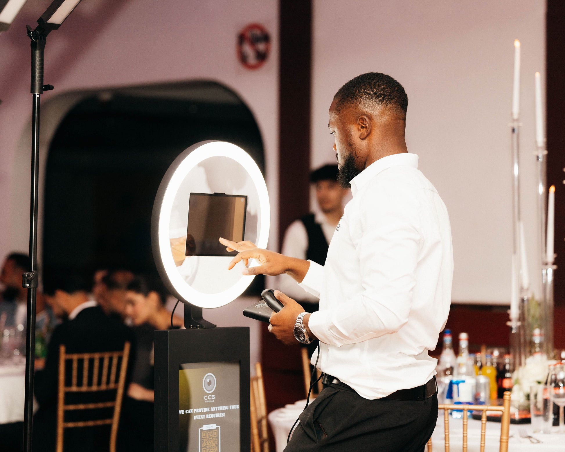 Man adjusting a ring light at an event with blurred attendees in the background