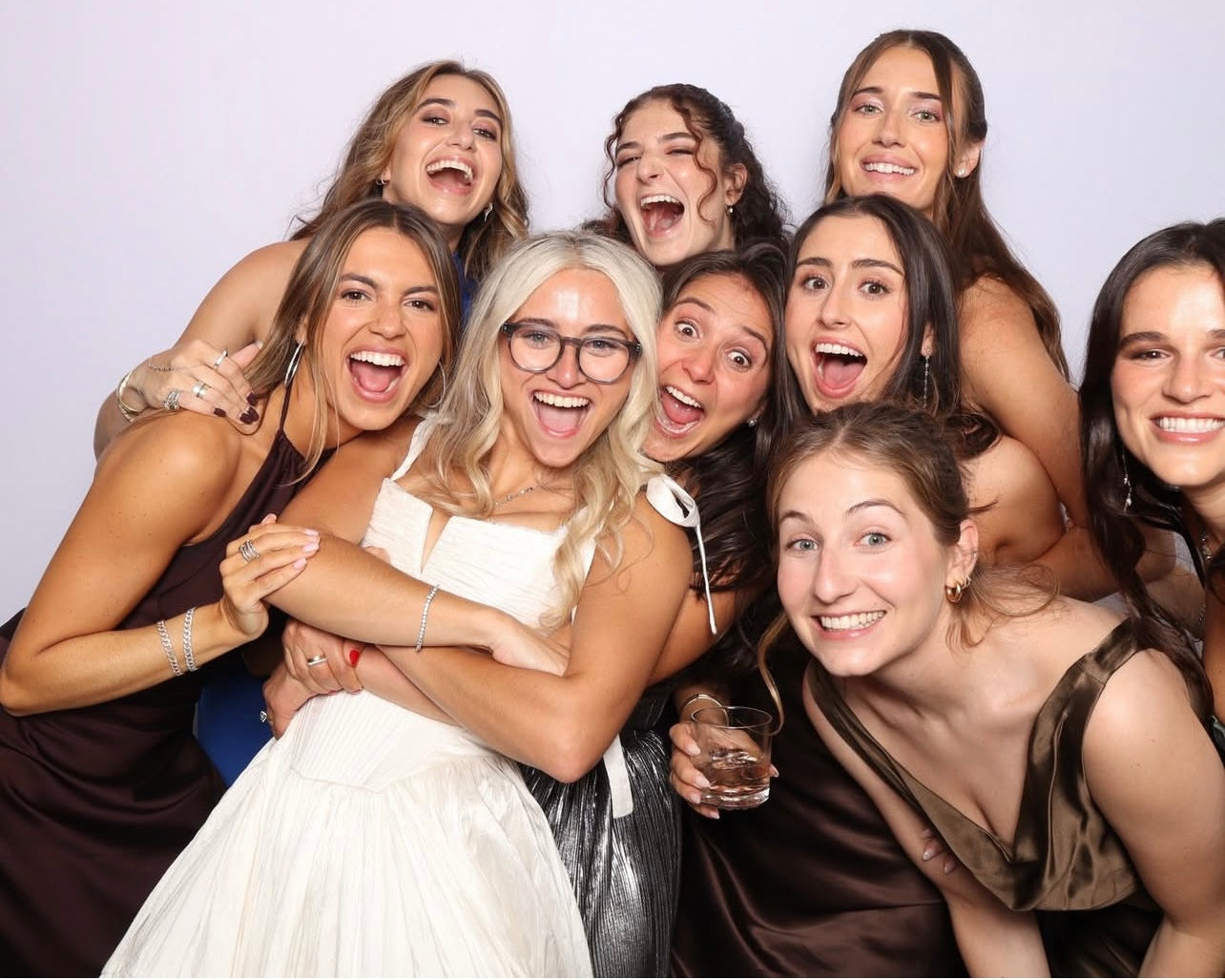Group of women posing together with a central woman in a white dress against a plain background