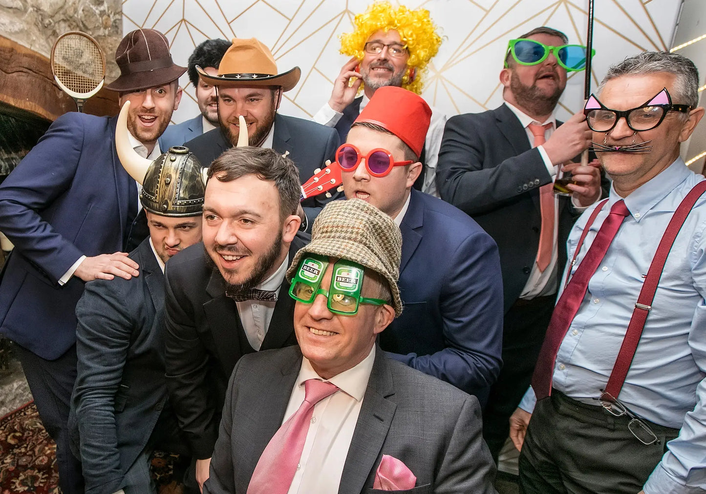 Group of men in formal attire with humorous accessories and props, including hats and glasses.