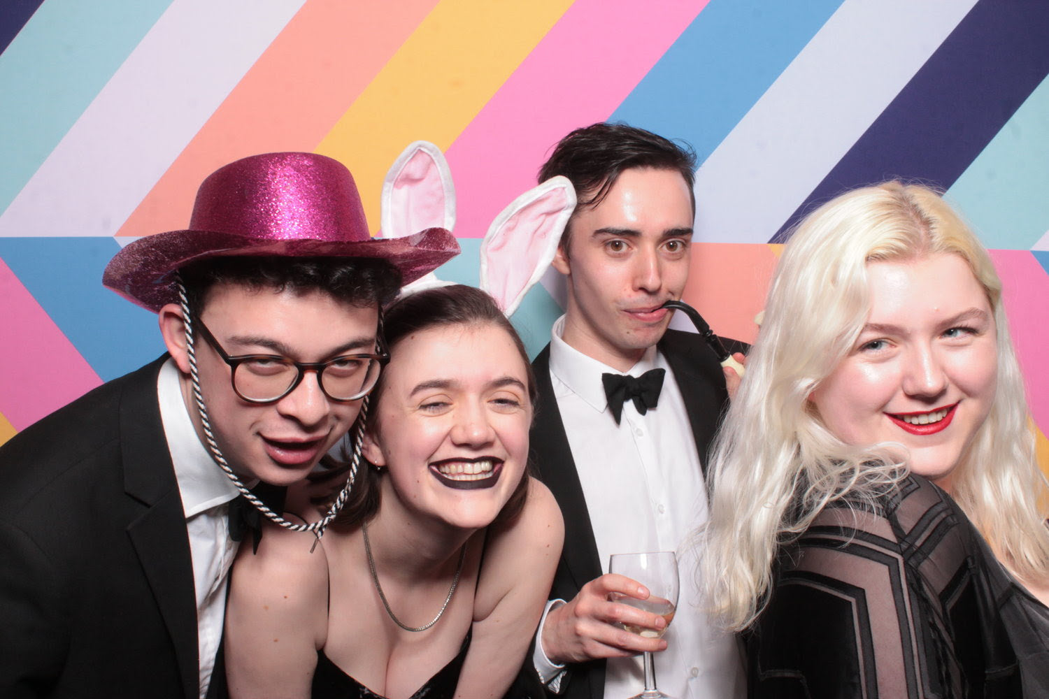 Four people in formal attire with bunny ears against a colorful striped background