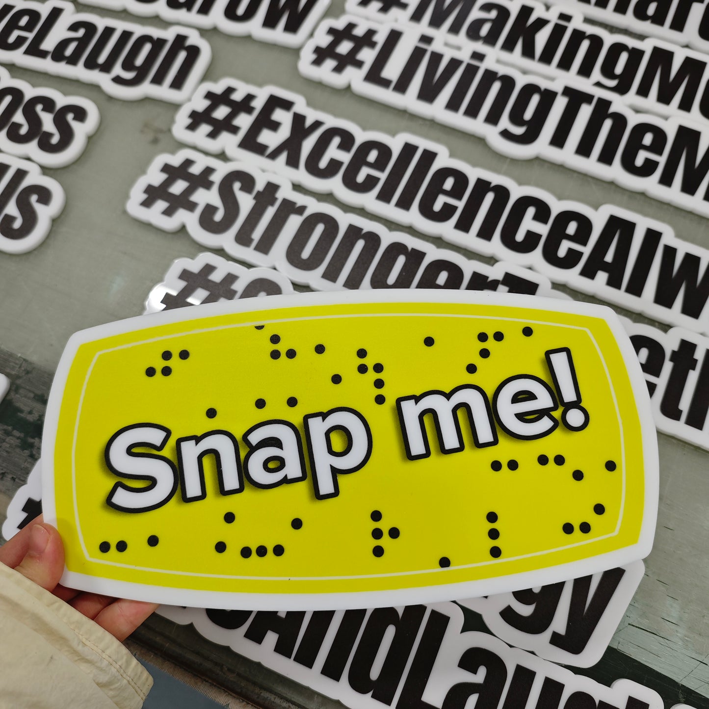 Yellow photobooth prop with 'Snap me!' text held by a hand, with other similar props in the background