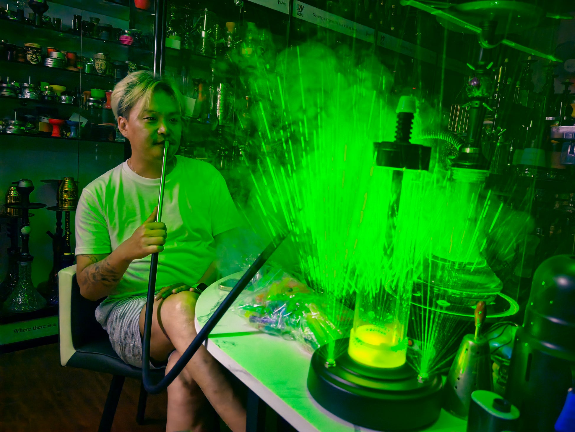 Man sitting at a table smoking from an  electric shisha pipe with green lasers shooting out.  