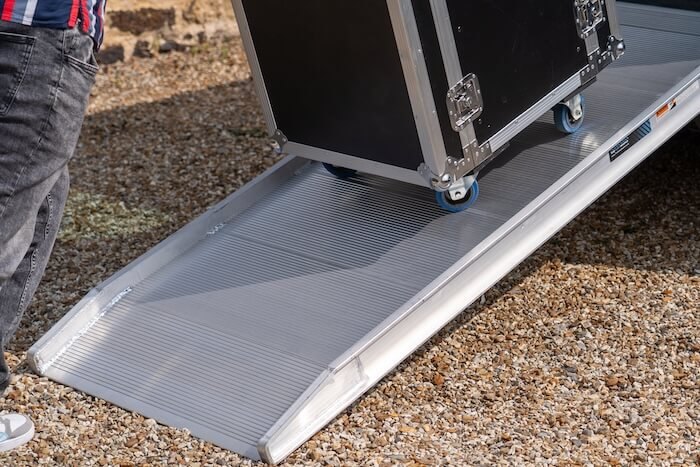 Sturdy aluminium Ramp being used to transport a large black flight case on a gravel surface