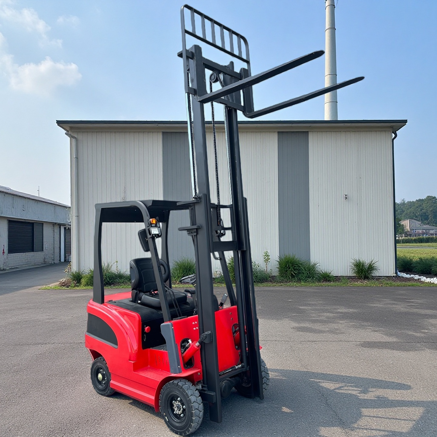 Red forklift with 4 wheels parked on a concrete surface with a building in the background