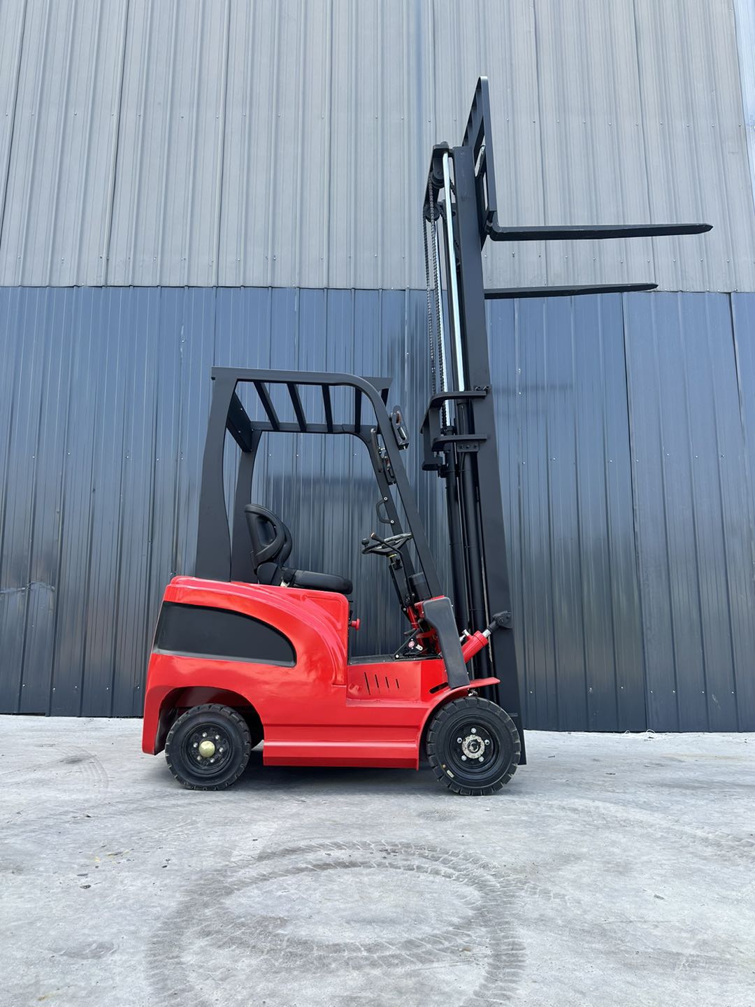 Red forklift with wheels in front of a grey industrial building