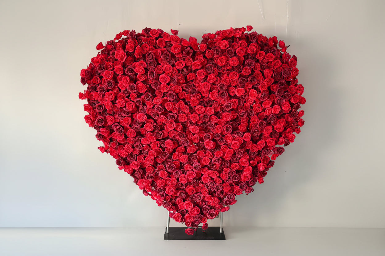Heart-shaped arrangement of red roses used for proposals and weddings set against a white curtain background