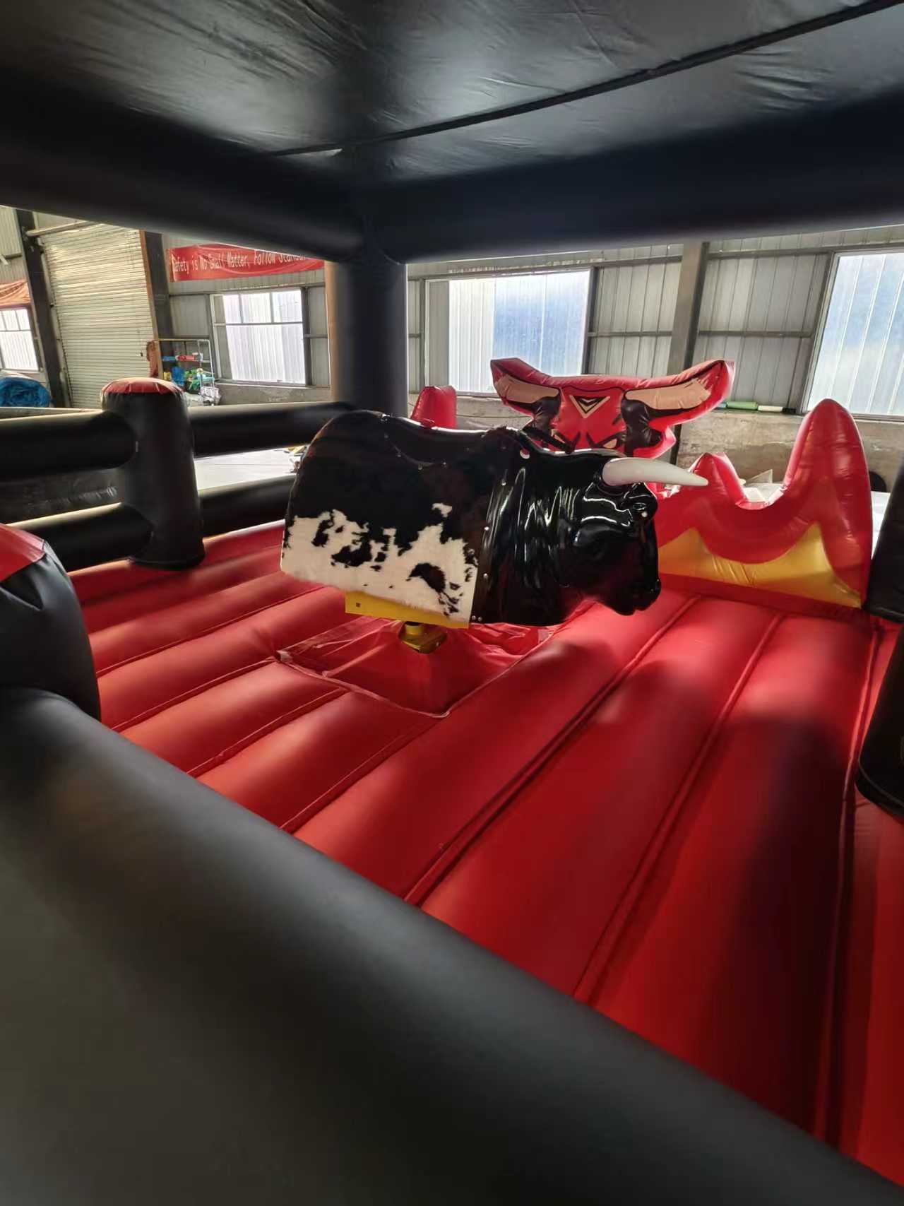 Inflatable mechanical bull ride with a cow print design on a red platform.
