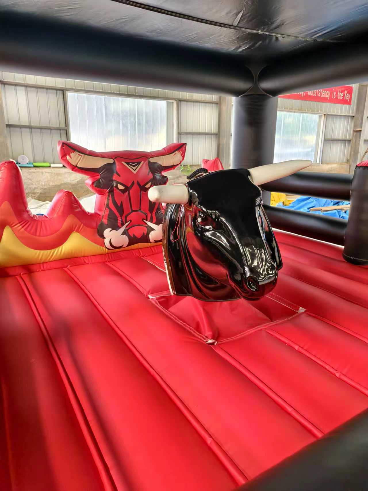 Inflatable bull machine with a black bull on a red inflatable platform in an indoor setting