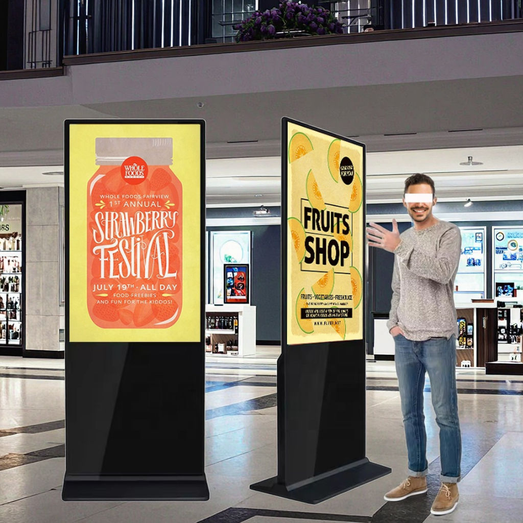 43” LED Touchscreen Indoor Digital Kiosk Floor Standing with promotional posters in a shopping mall, featuring a man interacting with one of them.